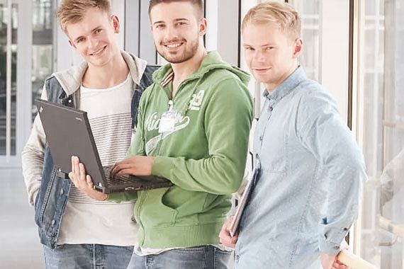 Drei ältere Schüler stehen mit einem Laptop auf einem Flur