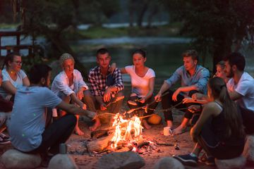 Eine Gruppe junger Erwachsener an einem Lagerfeuer beim Würstchengrillen