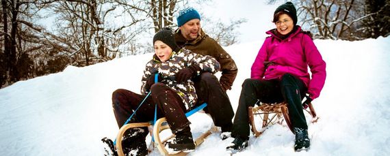Eltern und Kind rodeln einen schneebedeckten Waldhang hinunter und haben jede Menge Spaß.