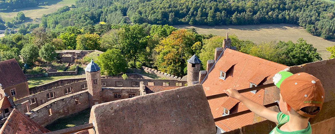 Kleiner Junge zeigt über die Dächer der Burg Breuberg in die Ferne 