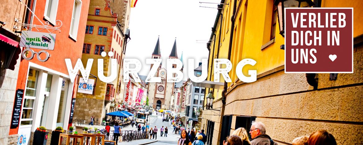 Eine volle Stadtkulisse mit Blick auf eine Kirche. Die umliegenden Häuser sind sehr bunt und in pastellfarben, also orange und rosa angestrichen. Die Beschriftung ist Würzburg und der Hinweis auf das Verlieb dich in uns Angebot befindet sich in der rechten Ecke.