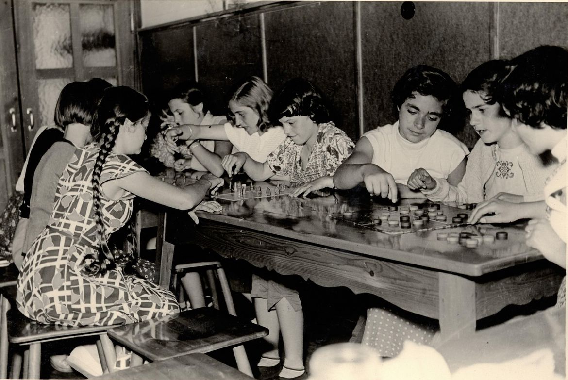 Schwarzweißfoto einer Gruppe Jugendlicher, die an einem Tisch sitzen und aktiv verschiedene Freizeitaktivitäten ausüben