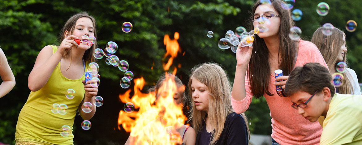 Jugendliche stehen an einem Lagerfeuer und machen Seifenblasen