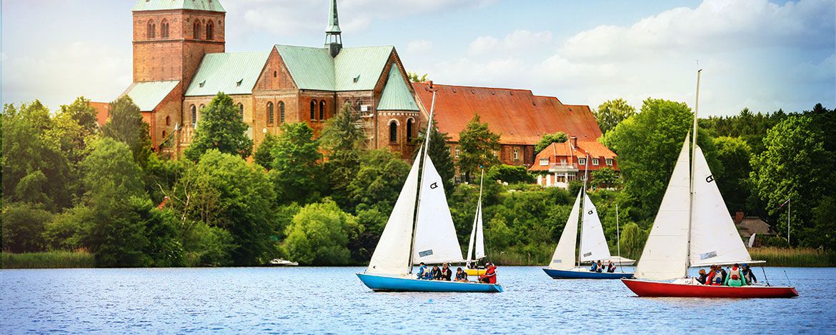 Drei Segelboote auf einem See vor einer Kirche