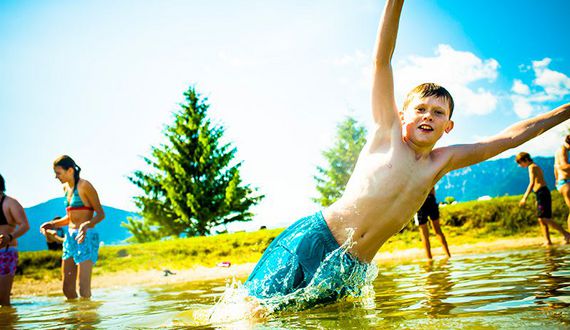 Badegäste in einem See, ein Kind im Zentrum des Bildes springt zur Seite ins Wasser