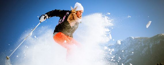 Dynamisches Foto einer Frau auf Skiern, um die herum der Schnee hoch aufwirbelt