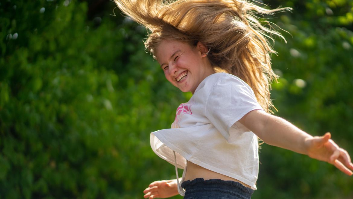 Ein hochspringendes Mädchen lacht mit wehendem Haar in die Kamera