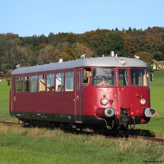 Ein roter Nostalgietriebwagen auf einem Gleis mitten in grüner Natur