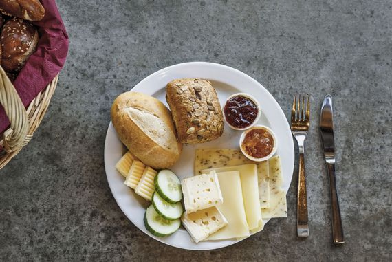 Ein Frühstücksteller mit Semmeln, Butter, Marmelade, Käse und Gurkenscheiben