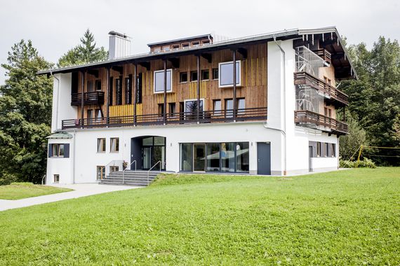 Aussenansicht der Jugendherberge Berchtesgaden, das modernisierte Haus Untersberg. Mit Holz verkleidet von außen und großen Fenstern.