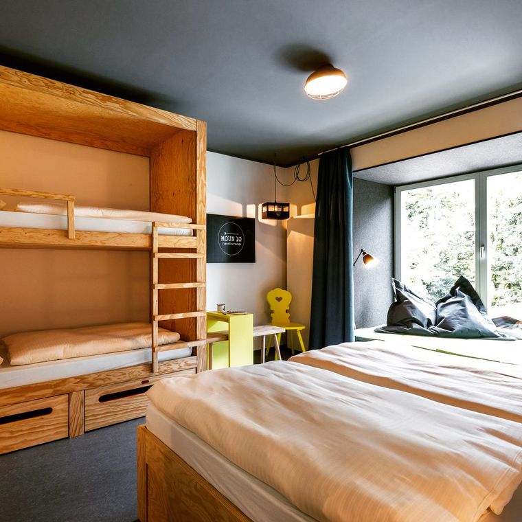Blick in ein Zimmer der Jugendherberge mopun10 in Garmisch-Partenkirchen mit einem Doppelbett und einem Etagenbett.
