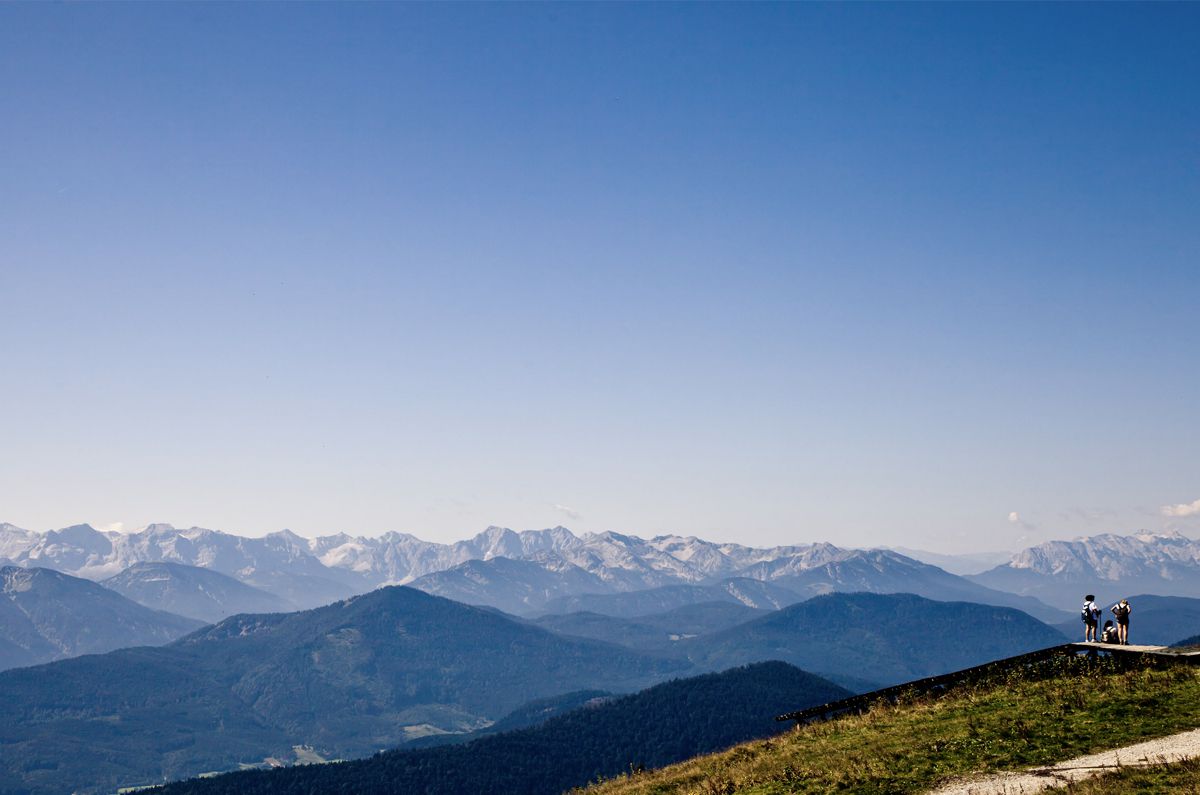Blick über die Gipfel der Alpen. Das Foto wird zu zwei Drittel von einem wolkenlosen blauen Himmel dominiert. Ganz unten rechts sieht man auf dem Foto eine kleine Gruppe von Menschen.