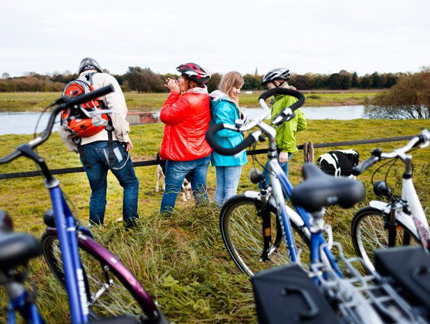 Eine vierköpfige Familie macht während ihrer Radtour am Weserradweg eine Pause und schaut sich den Fluss an