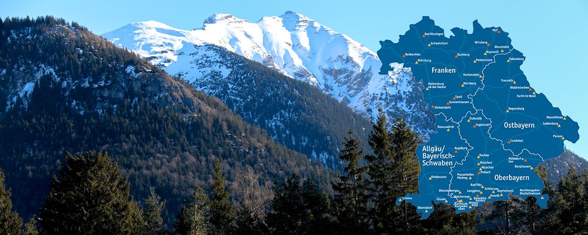 Panoramablick über schneebedeckte Berge in den bayerischen Alpen, im Vordergrund Teil eines Nadelwalds