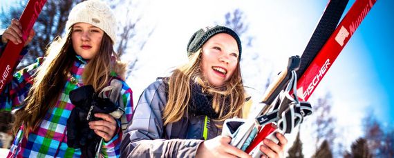 Zwei junge Mädchen in Skisachen und mit Skiern in der Hand