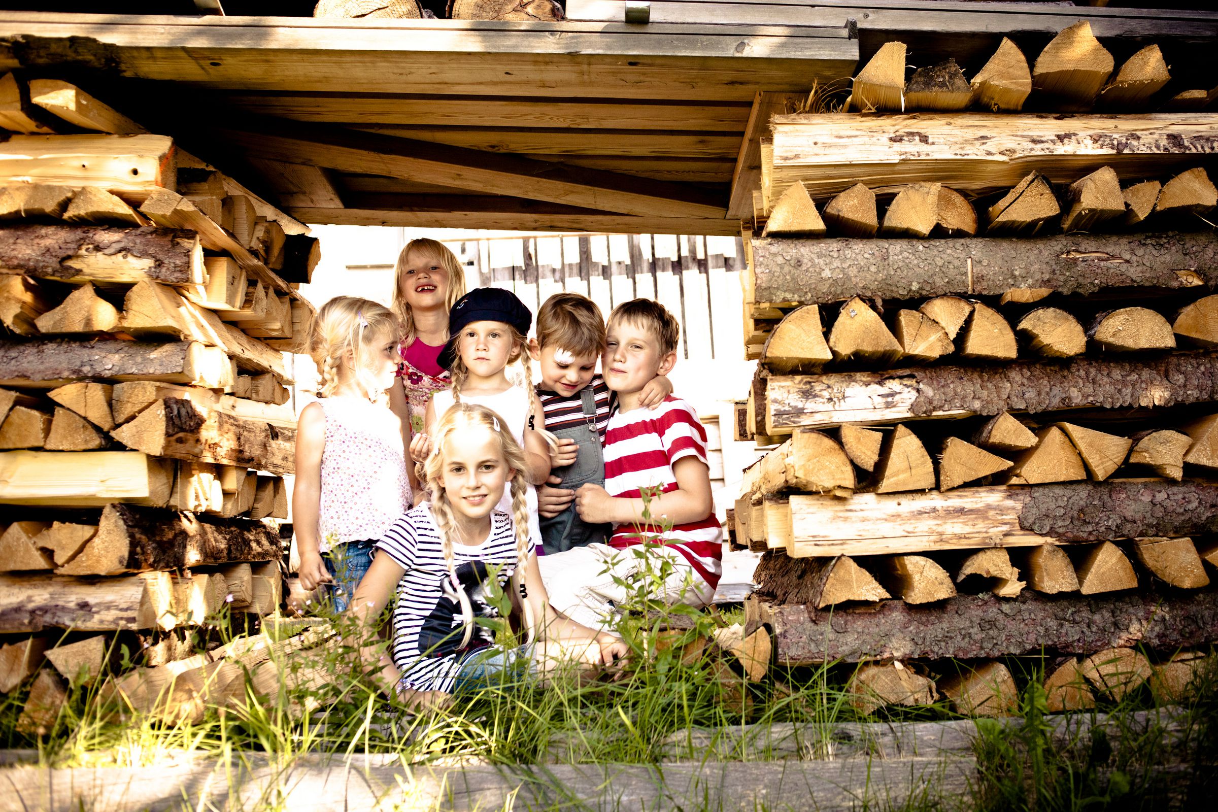 Eine Gruppe Kinder zwischen aufgeschichteten Holzstapeln.