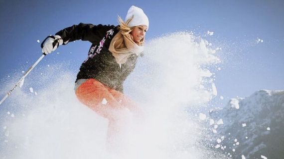 Dynamisches Foto einer Frau auf Skiern, um die herum der Schnee hoch aufwirbelt