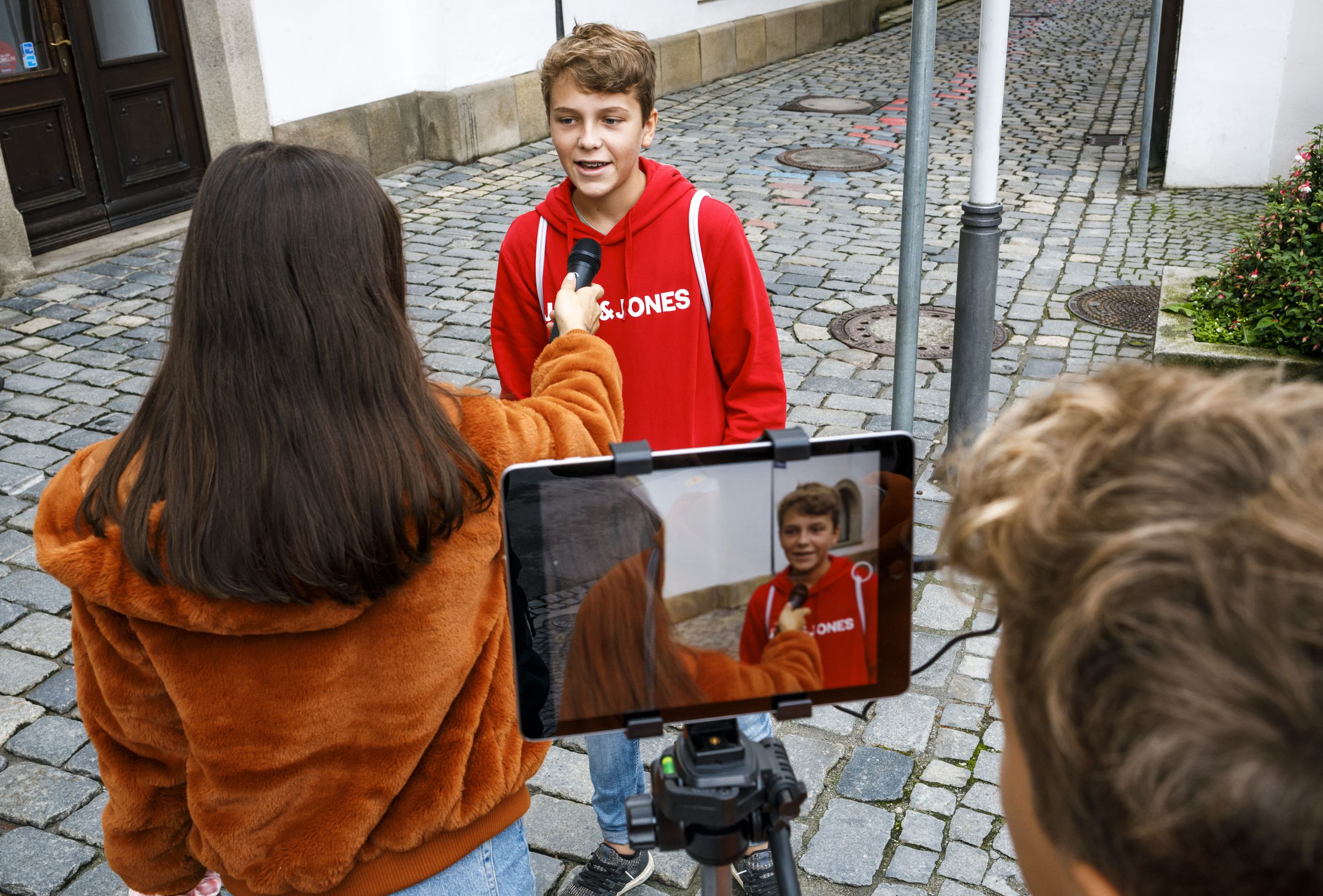 Zwei Schüler machen ein Interview. Im Vordergrund sieht man ein Tablet auf einem Stativ, das als Kamera dient.