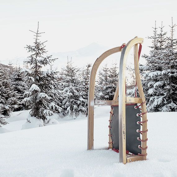 Ein senkrecht aufgestellter Schlitten in einer Schneelandschaft mit einem Wald im Hintergrund