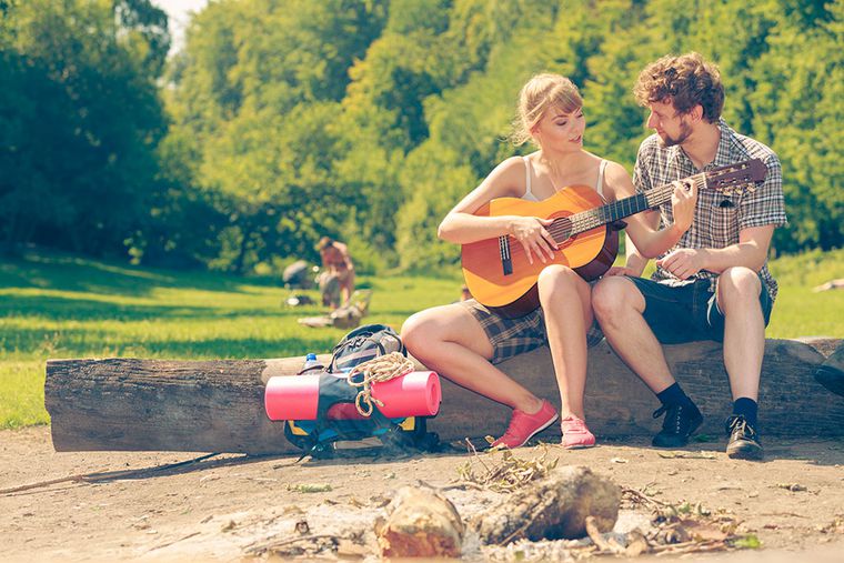 Ein Mann und eine Frau sitzen auf einem Baumstamm, sie spielt Gitarre