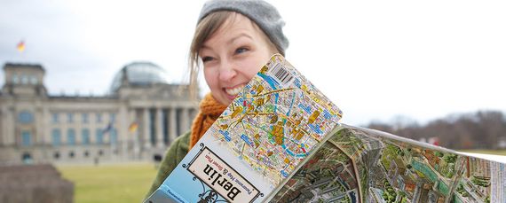 Eine junge Frau steht vor dem Reichstag in Berlin und hat einen Stadtplan in der Hand.