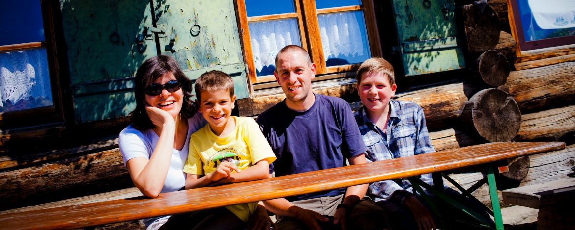 Eine Familie mit vier Personen sitzt auf einer Bierbank und sieht fröhlich in die Kamera