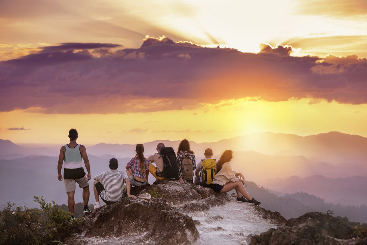 Das Foto zeigt eine Gruppe von sieben Menschen auf einem Berg, die ins neblige Tal hinunterschauen und den Sonnenuntergang genießen