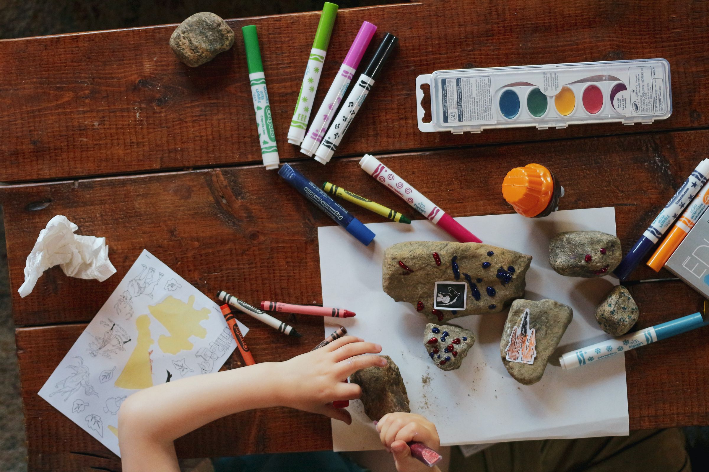 Ein Tisch mit Farbstiften, Malfarben, Steinen und Dekorsteinchen als Symbol für das Selbermachen