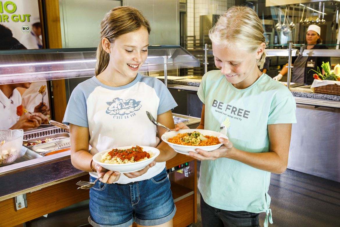 Zwei Kinder am Essensbuffet zeigen sich gegenseitig ihre vollen Teller