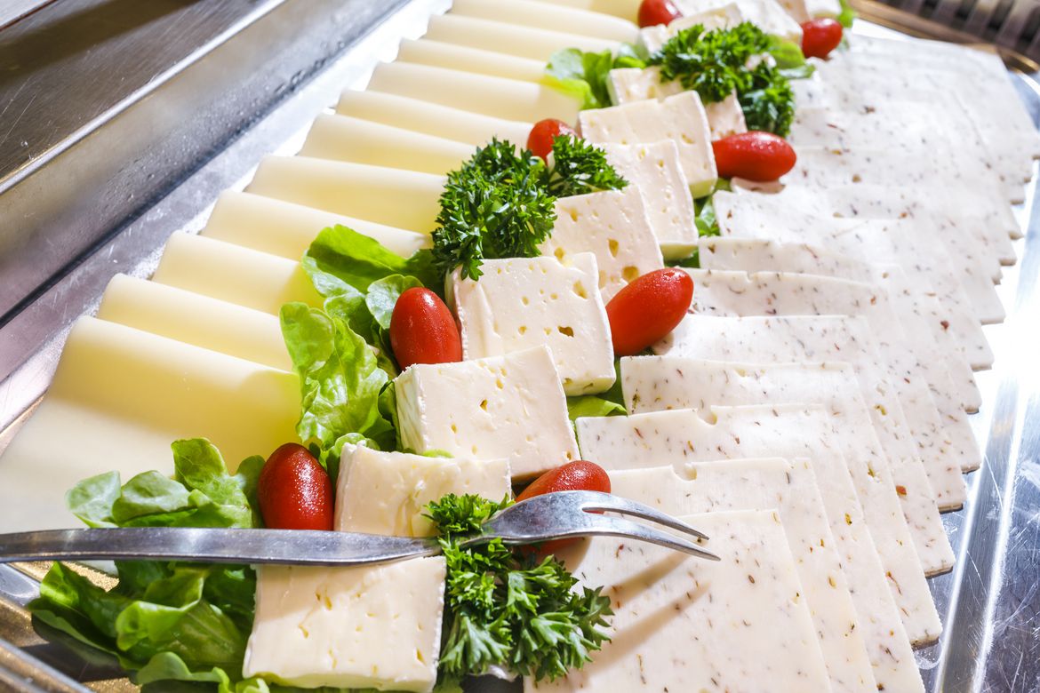 Metalltablett mit einer Auswahl von drei unterschiedlichen Käsesorten, dekoriert mit einigen Petersilie, Salat und Tomaten.