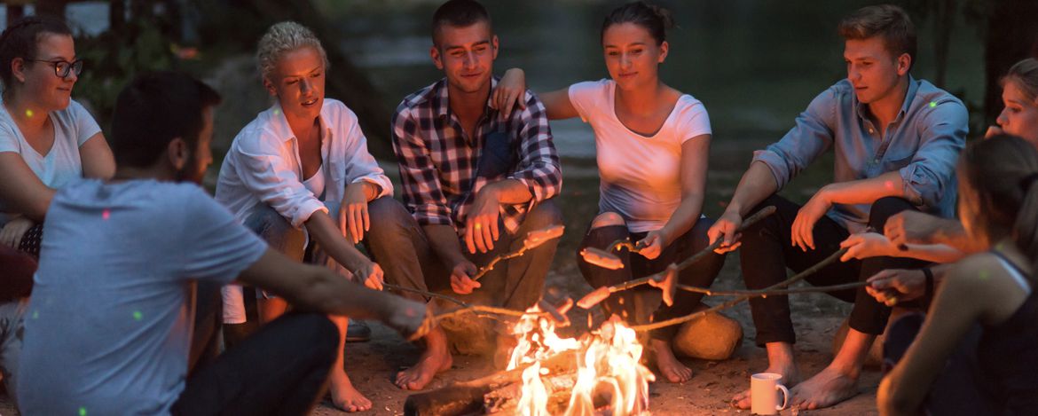 Eine Gruppe junger Erwachsener an einem Lagerfeuer beim Würstchengrillen
