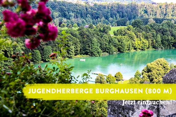 Blick über den Wöhrsee. Das Foto wird überlagert von dem Schriftzug "Jugendherberge Burghausen - jetzt eintauchen".