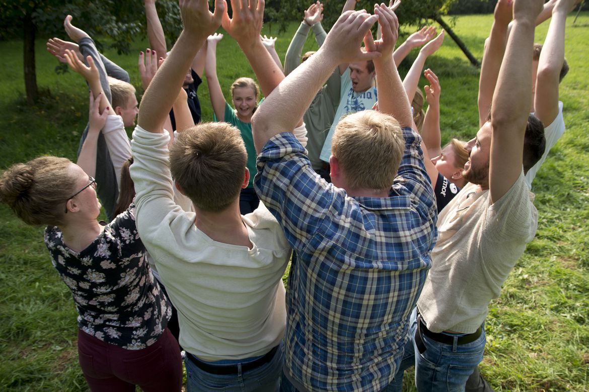 Eine Gruppe junger Menschen steht im Kreis und wirft lachend die Arme über den Kopf