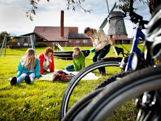 Im Vordergrund sieht man unscharf einige Fahrräder im Huntergrund ist eine vierköpfige Familie die auf einer Picknickdecke sitzt.