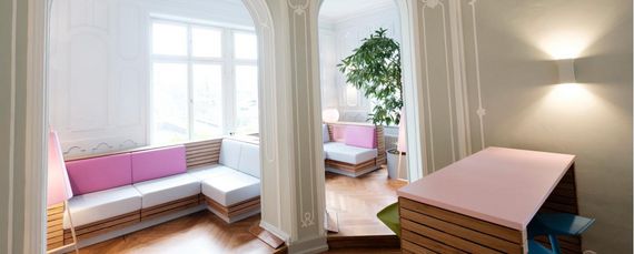 Öffentlicher Sitzbereich in der Jugendherberge Lindau mit Sitzelementen in Holzoptik und mit weißen sowie rose-farbenen Lederauflagen.