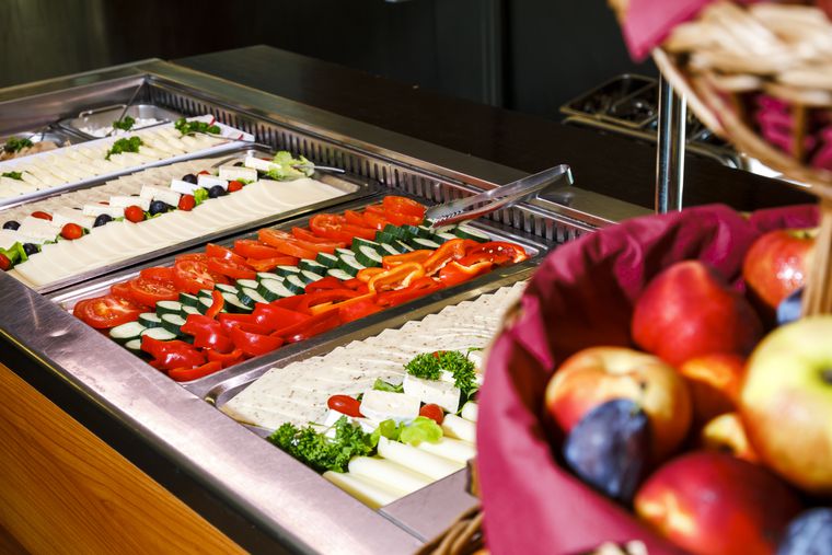 Foto des Buffets mit einer Auslage von Gemüse und Käse. Vorne rechts ein unscharfer Obstkorb.
