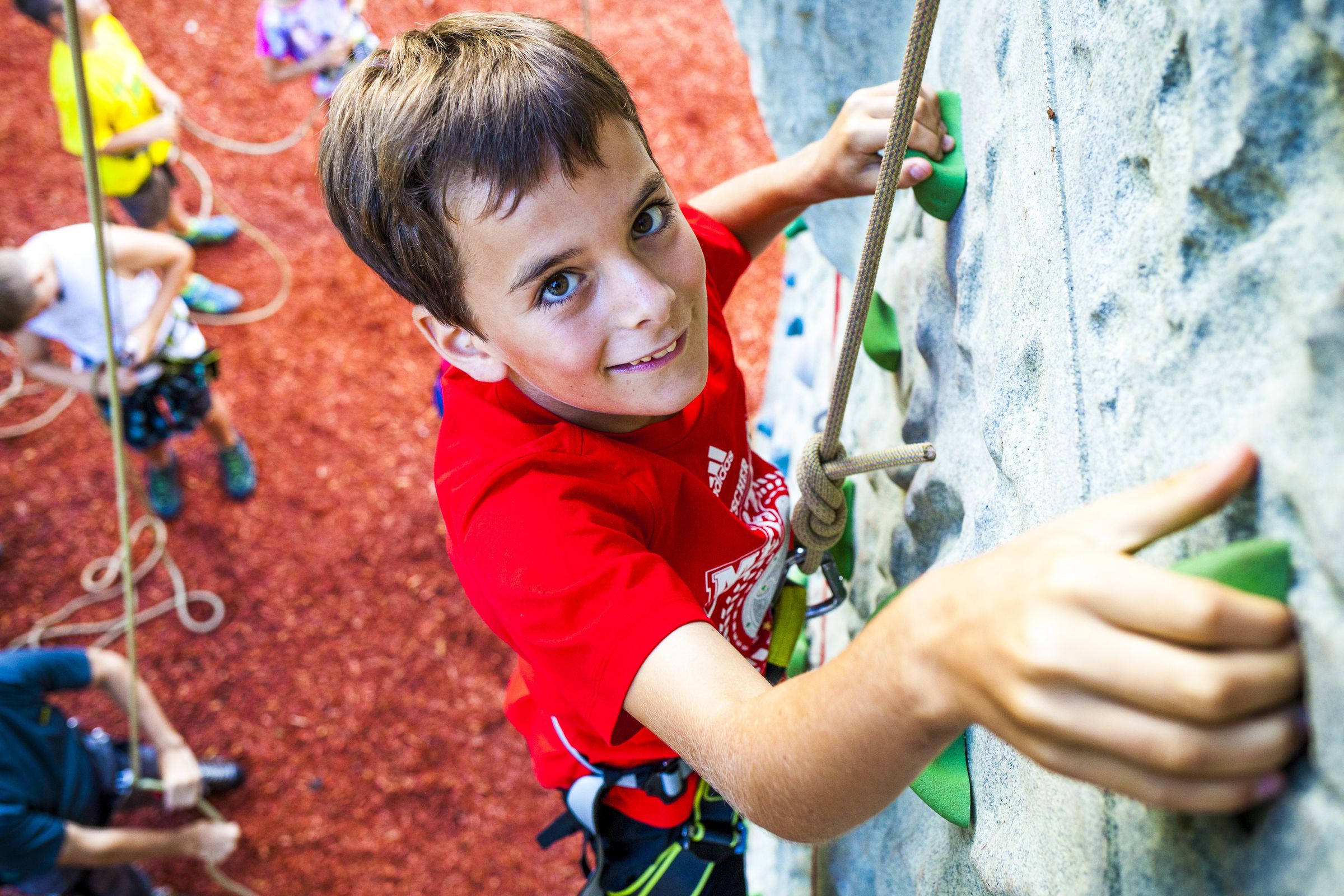 Eine Junge klettert grinsend eine Kletterwand hoch