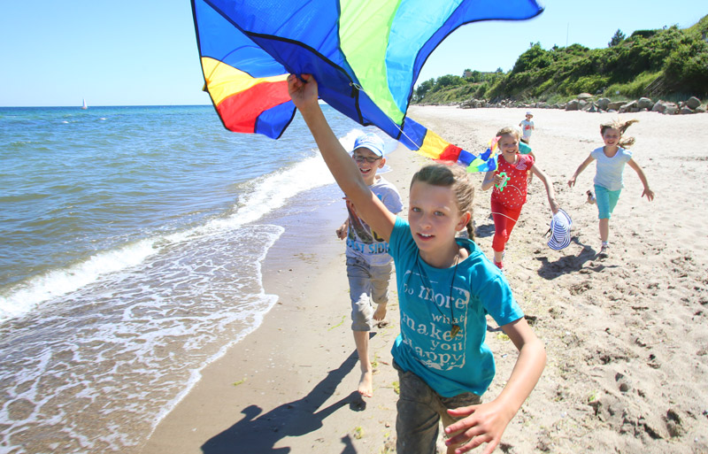 Kinder spielen im Familienurlaub am Meer mit einem bunten Drachen am Strand