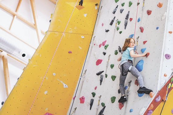 Eine Kletterwand in einer Kletterhalle in der ein Kind klettert. 