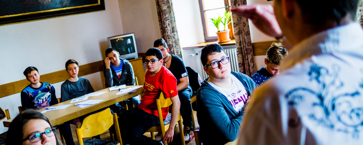 An Tischen sitzende Jugendliche hören einem Workshop-Leiter zu