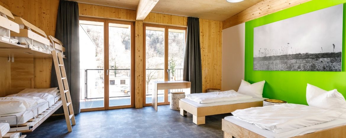 Blick vom Holzstockbett ins großzügige Zimmer mit Sitzhockern und hellen Holzmöbeln