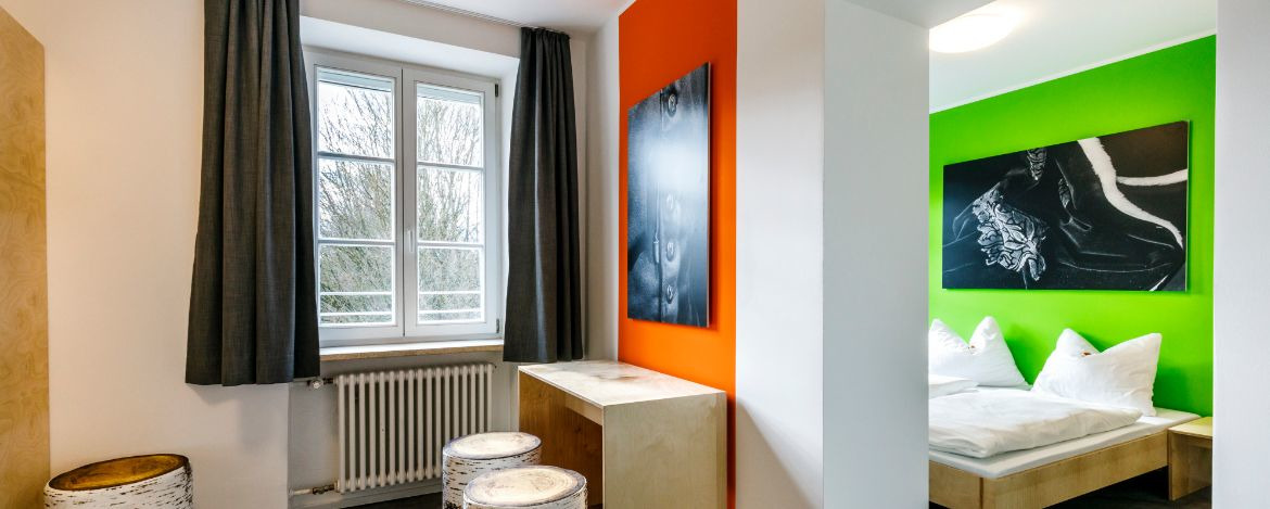 Modernes Mehrbettzimmer in der Jugendherberge Burghausen mit Sitzmöglichkeiten und farbigen Wänden