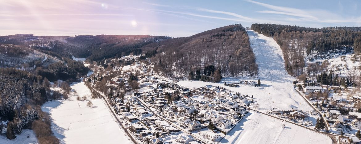 Flight over the vacation resort in Willingen in Hesse. Gastronomy and vacation houses are located next to downhill ski slopes.