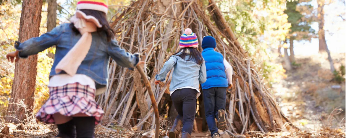 Three kids play outside shelter made of branches in a forest